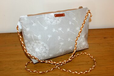 Grau-beige genähte Tasche mit Reißverschluss, weißem Pusteblumenprint und geflochtenem braun-beigem Trageriemen