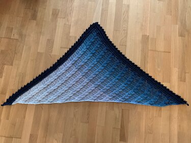 Triangle crochet shawl laid flat showing blue gradient, raised textured rows and navy scalloped edging