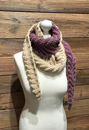 Gehäkelter Schal in Beige und Lila mit Zopfmuster auf weißer Schaufensterpuppe vor Holzwand