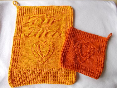Zwei gestrickte Topflappen in Gelb und Orange mit Herzmotiv, geripptem Rand und Aufhängeschlaufen