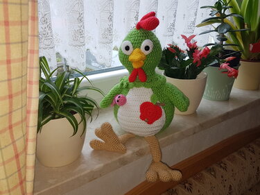 Gehäkeltes grünes Amigurumi-Huhn mit rotem Kamm und Apfel-Applikation auf Fensterbank