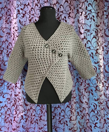 Beige-graue gehäkelte Damenjacke mit V-Ausschnitt, schräger Knopfleiste und 3/4-Ärmeln auf Mannequin