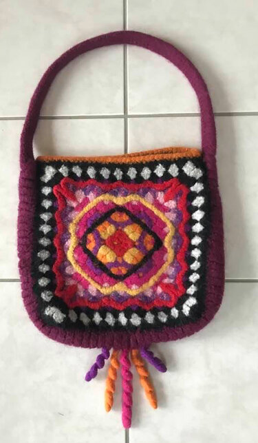 Bunte gehäkelfilzte Tasche mit zentralem Granny‑Square‑Muster und Quasten