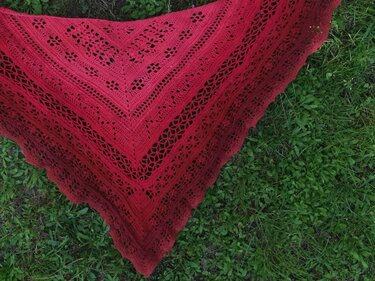 Rotes gehäkeltes Dreieckstuch mit Lochmuster und Farbverlauf, ausgebreitet auf grünem Gras.
