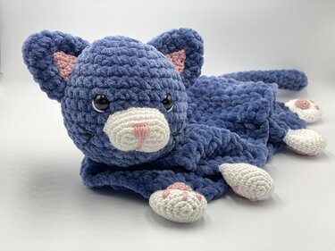Blue crocheted cat snuggle blanket with plush head, tail and white paws with pink pads on a white background