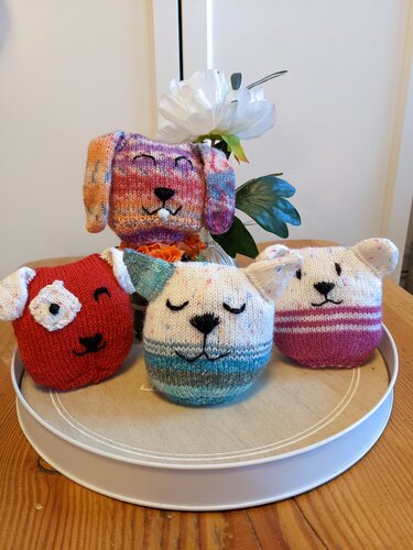 Vier handgestrickte Amigurumi-Tierköpfe (Hase und Hunde) auf einem runden Tablett.