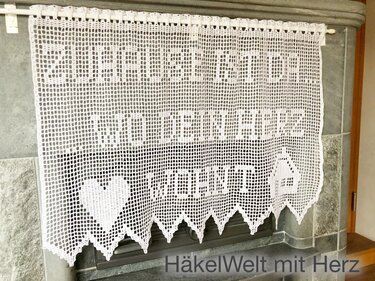 Weiße Filet-Häkelgardine mit Spruch 'Zuhause ist wo dein Herz ist', Herzmotiven und gezacktem Saum