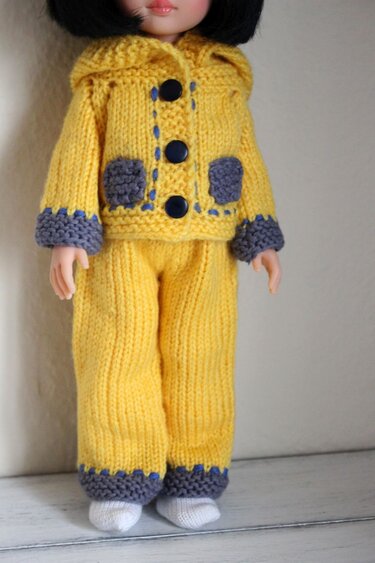 Doll wearing a yellow hand-knitted hooded jacket with three buttons and matching yellow pants with grey trim