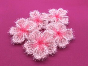 Fünf kleine flauschige rosa Häkelblüten mit dunklerer Mitte auf kräftigem Pink