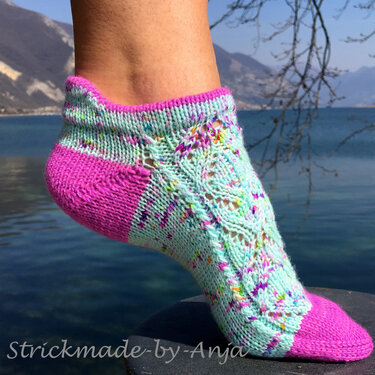 Gestrickte Knöchelsocke in Mint mit pinker Ferse und Ajourmuster vor Bergsee-Kulisse