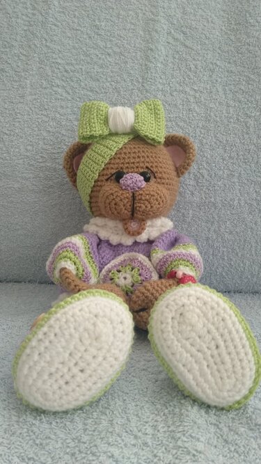 Nahaufnahme gehäkelter Teddybär mit weißen Sohlen, gestreifter Jacke und grüner Stirnschleife