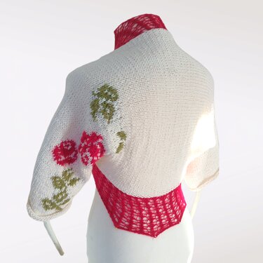 Kurz gestrickter cremefarbener Damen‑Bolero mit rotem Netzeinsatz im Rücken und Rosenintarsia am Ärmel auf einer Schaufensterpuppe
