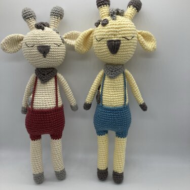 Zwei gehäkelte Giraffen-Amigurumi in Creme und Hellgelb mit geschlossenen Augen, Halstüchern und Hosenträgern