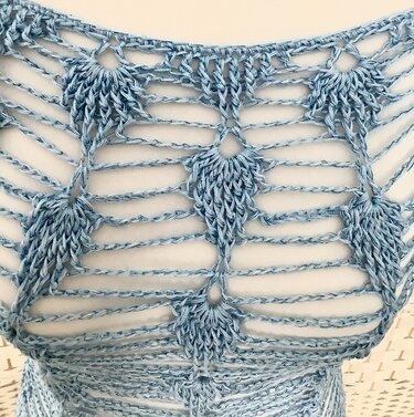 Detailaufnahme eines hellblauen gehäkelten Damen-Tops mit offenen Luftmaschenreihen und Muschelfächern