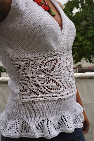 Weißes gestricktes Damentop mit V‑Ausschnitt, Ajourmuster in der Taille und gewelltem Saum, an einer Person getragen