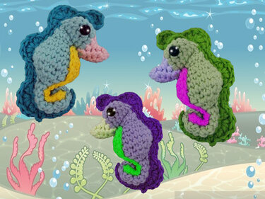 Drei gehäkelte Seepferdchen in Türkis, Hellgrün und Violett vor einem blauen Unterwasser-Hintergrund.