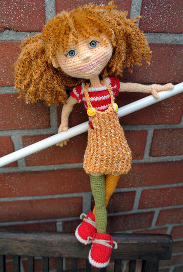 Crocheted amigurumi girl doll in orange pinafore and striped top