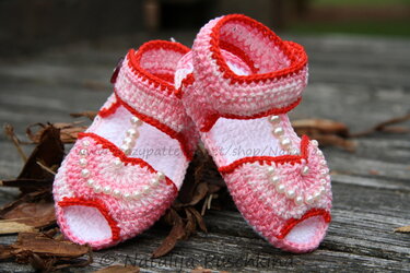 Gehäkelte Babysandalen in Rosa und Weiß mit roten Kanten und Perlen auf Holz