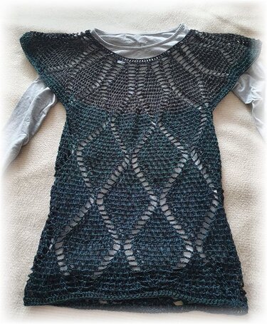 Dunkelgrüne, gehäkelte Damen-Tunika mit offenem Rautenmuster über einem grauen Langarmshirt.