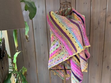 Mehrfarbiges gehäkeltes Dreieckstuch auf Schneiderpuppe mit Streifen- und Lochmustern in Pink, Gelb und Violett.