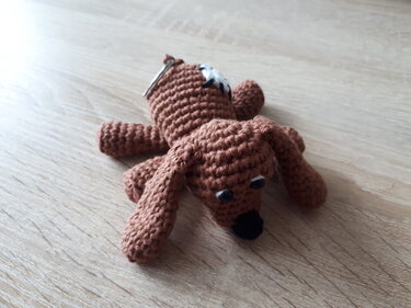 Brauner gehäkelter Hunde-Schlüsselanhänger mit Schlappohren auf Holzfläche