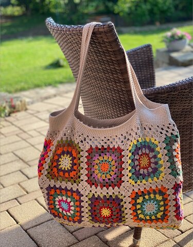 Handgehäkelter Shopper mit bunten Granny Squares an einem Korbstuhl im Garten hängend