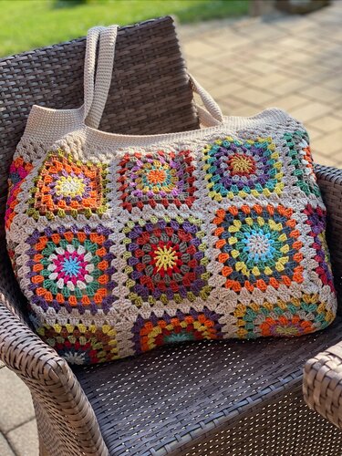 Gehäkelter Shopper mit neun bunten Granny‑Squares und beigen Trägern auf einem Gartenstuhl