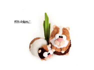 Zwei gehäkelte Amigurumi‑Meerschweinchen, braun-weiß, mit rosa Nase und grüner Blattdekoration