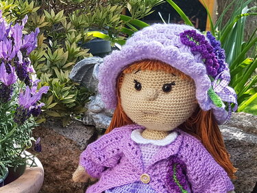 Handgehäkelte Puppe mit rotbraunem Haar, lila Hut und passendem Cardigan neben Lavendel