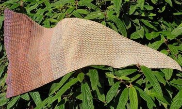 Gehäkeltes Tuch in Erdtönen und Lila auf grünen Blättern