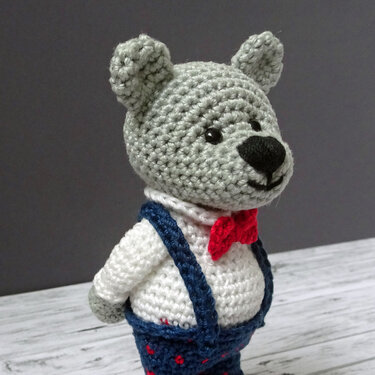 Gehäkelter grauer Teddybär mit roter Fliege und blauen Hosenträgern