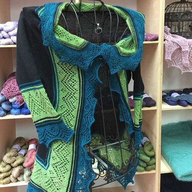 Women's knit cardigan with green openwork, blue trim and black sleeves on a display form.