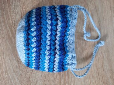 kleine gehäkelte beuteltasche mit blauen und weißen streifen und kordelzug auf holzuntergrund