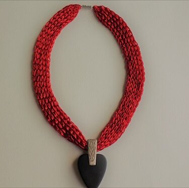 Rote gestrickte Halskette mit schwarzem Herzanhänger auf hellem Hintergrund
