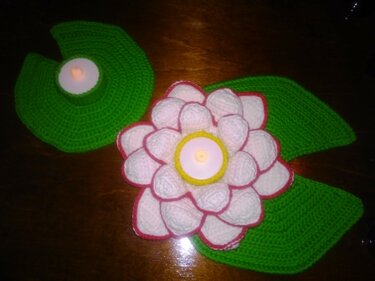 Zwei gehäkelte Teelichthalter: Eine weiße Seerosenblüte mit rosa Rand und ein grünes Seerosenblatt, beide mit Teelichtern.