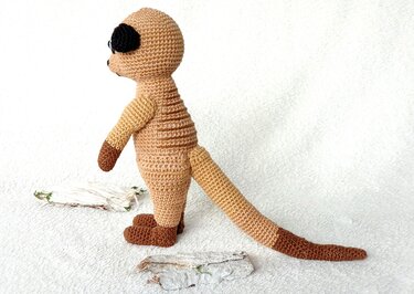 Gehäkeltes Erdmännchen in Beige- und Brauntönen, seitliche Ansicht auf hellem Hintergrund.