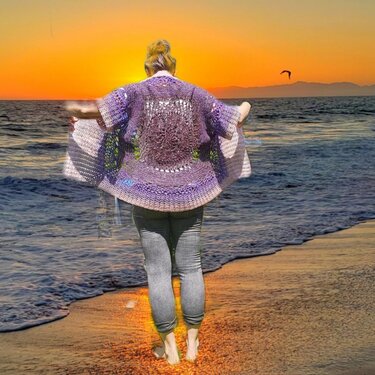 Frau barfuß am Strand mit lila Häkeljacke im Kimono‑Stil und rundem Rückenmotiv