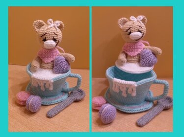Gehäkelte Amigurumi-Katze auf weißem Deckel in hellblauer Teetasse mit gehäkelten Macarons und Löffel
