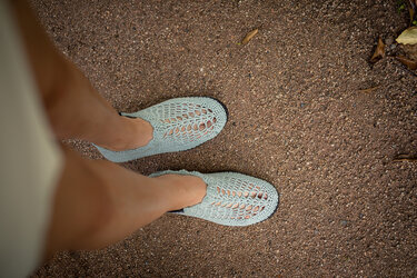 Draufsicht auf hellmintfarbene, gehäkelte Sommerschuhe mit offenem Muster und dunkler Sohle