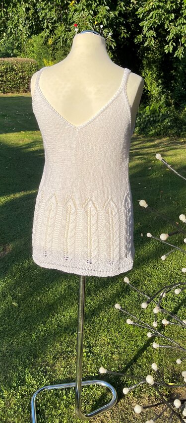 Rückansicht eines hellen Strick-Tops mit V-Rücken und vertikalem Muster am Saum, auf einer Schneiderpuppe im Garten.