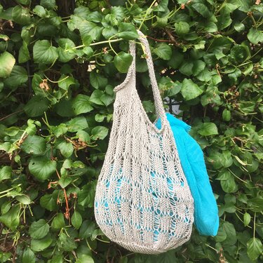 Beige gestrickte Netztasche mit türkisem Tuch vor grüner Hecke