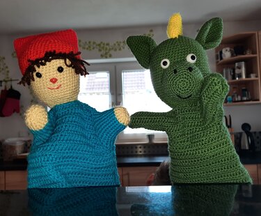 Gehäkelte Handpuppen: Junge mit roter Mütze und grüner Drache nebeneinander