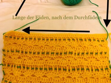Detail einer gelben Häkelarbeit mit grünem Garn, das durch die Reihen gezogen wird als Arbeitsschritt.