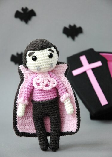 Crocheted vampire amigurumi in black and pink with ruffled collar and pink-lined cape