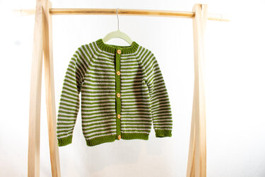 Grün-weiß gestreifte Kinderstrickjacke mit Holzknöpfen an einem Holzständer
