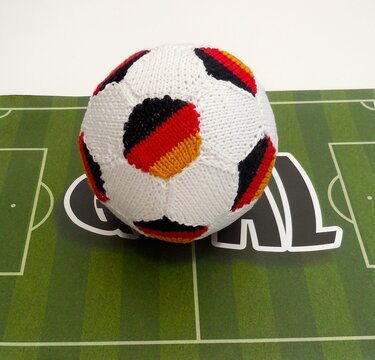 Handgestrickter weicher Fußball in Schwarz, Rot und Gold auf grüner Fußballfeld-Unterlage
