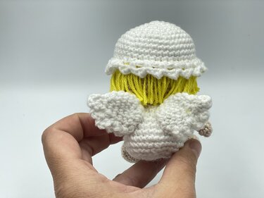Rear close-up of a small amigurumi crochet angel showing wing shaping, scalloped hat and yellow yarn hair