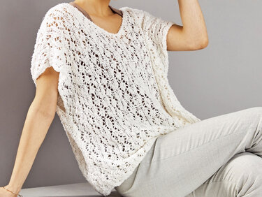 Weißer, locker gestrickter Damenpullover mit V‑Ausschnitt und Lochmuster an sitzender Person