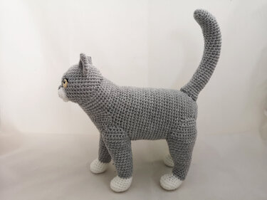 Gray crocheted amigurumi cat with white paws and upright tail