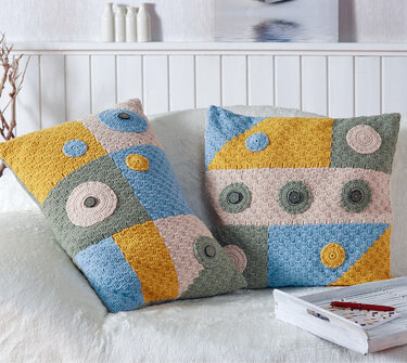 Zwei gehäkelte Patchwork-Kissenbezüge in Gelb, Blau, Rosa und Grün auf hellem Sofa